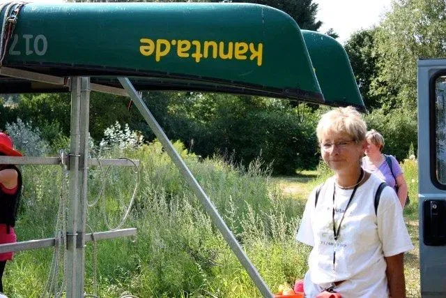 kanuverleih-kanutouren-kanuvermietung-kanuta-22 Eine Frau steht neben einem Kanu auf einem Feld.