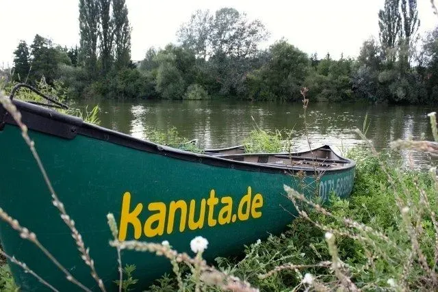 kanuverleih-kanutouren-kanuvermietung-kanuta-23 Ein grünes Kanu steht neben einer Rasenfläche.