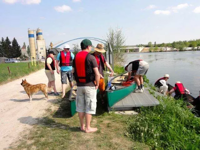Eine Gruppe von Menschen steht mit Kanus an einem Fluss.