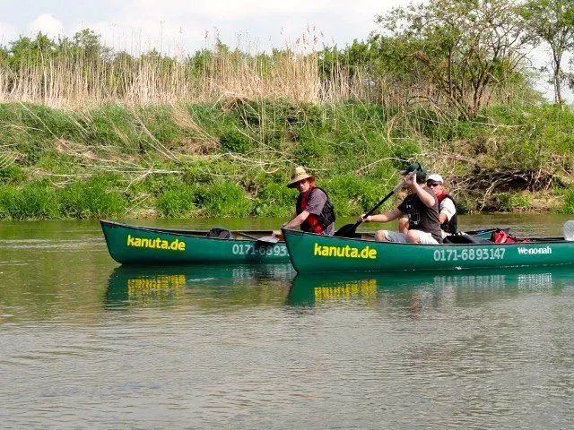 Zwei Menschen paddeln in Kanus einen Fluss hinunter.