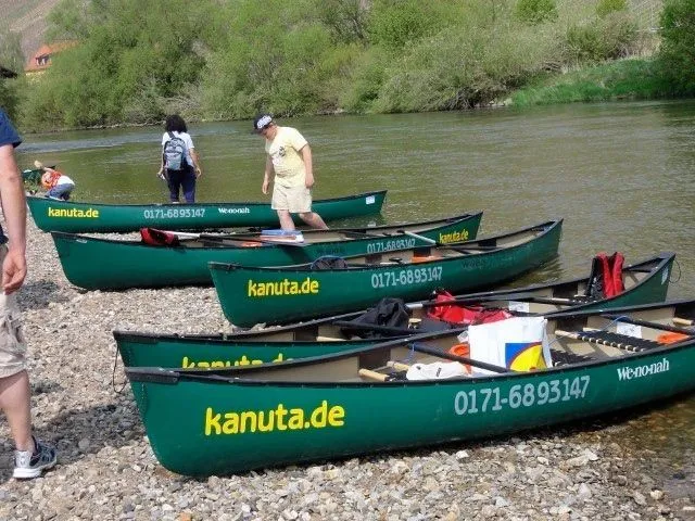Eine Gruppe von Menschen steht neben Kanus auf einem Fluss.