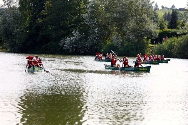 Eine Gruppe von Menschen paddelt in Kanus auf einem See.