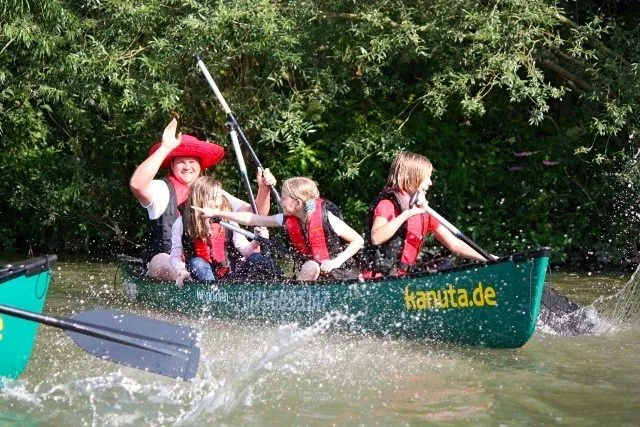 Eine Gruppe Kinder paddelt in einem Kanu auf einem Fluss.