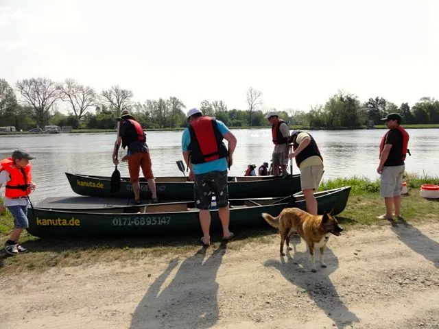 Eine Gruppe von Menschen steht mit einem Hund neben einem Kanu.