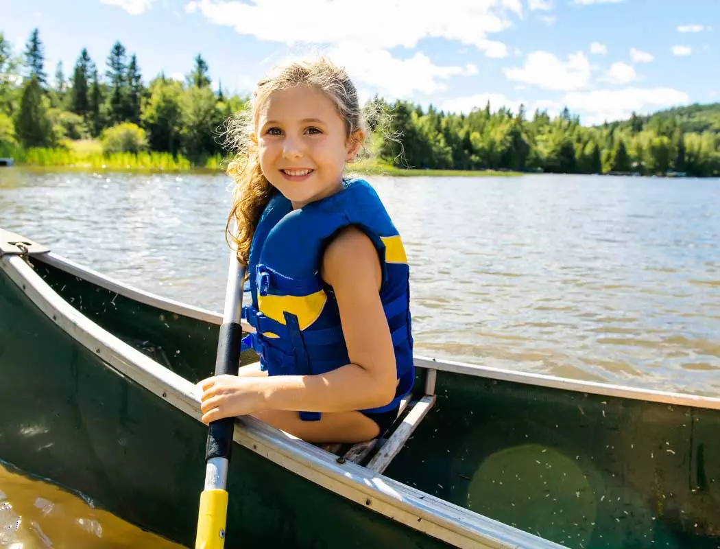 Ein junges Mädchen in einer Kanutouren-Schwimmweste paddelt mit einem Kanu auf einem See.